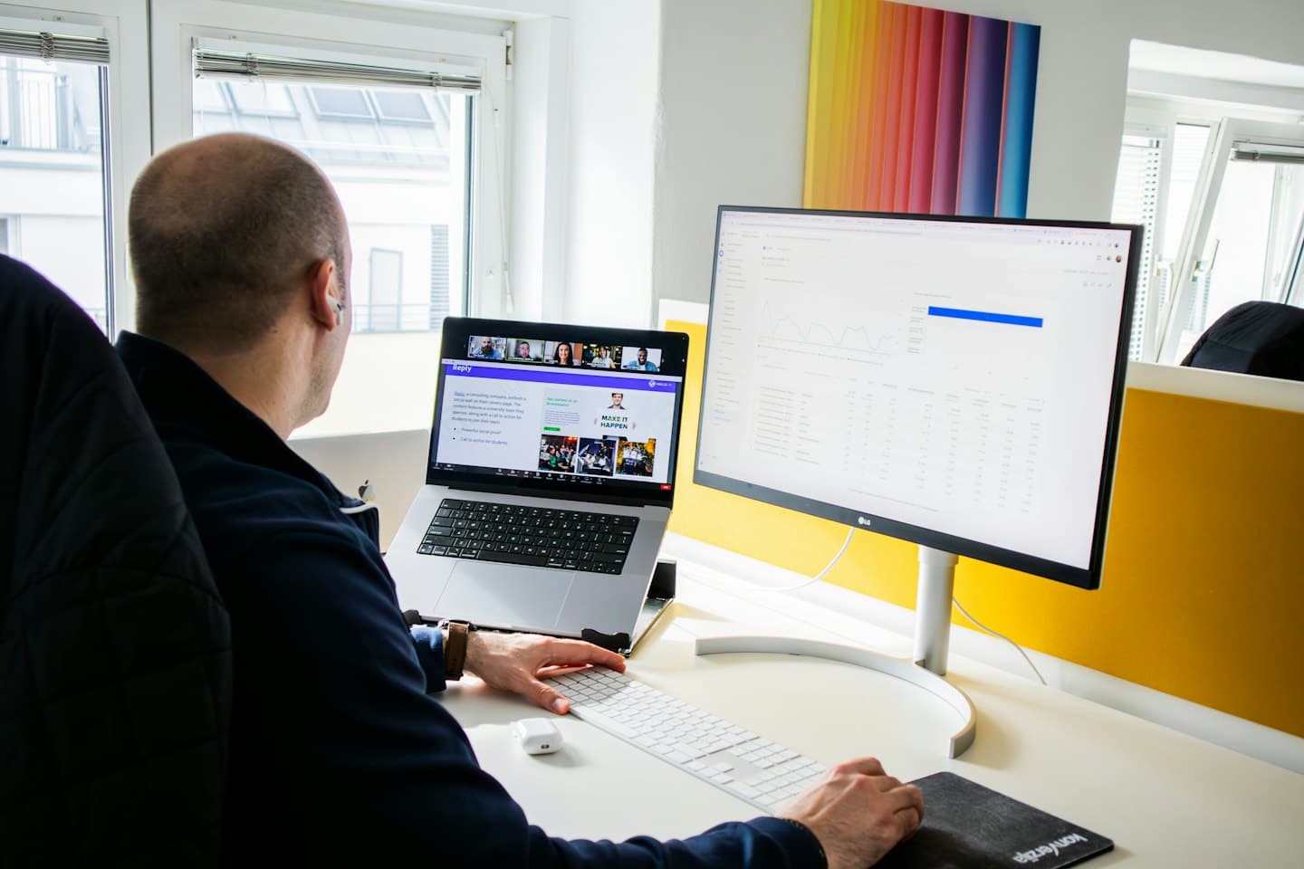 Mann jobber på bærbar PC og skjerm på et moderne kontor.